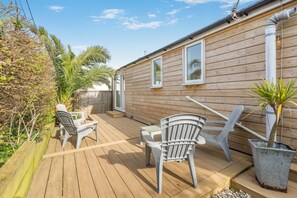A wooden deck with outdoor furniture, a potted plant, and a wooden building with windows.