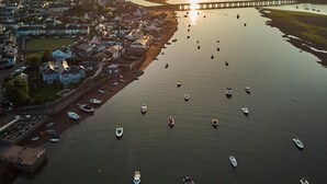 Eine Küstenstadt mit einem Hafen voller Boote, einer Brücke im Hintergrund und Häusern entlang der Uferlinie.