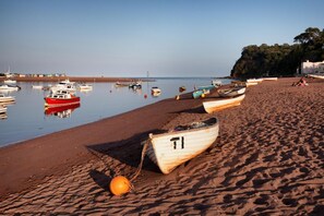 A beach with boats, a lighthouse, and a building in the background.