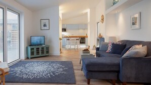 Ein modernes Wohnzimmer mit einer Couch, einem Fernseher und einem Essbereich im Hintergrund.