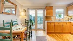 A kitchen with wooden cabinets, a dining table with chairs, and a sliding glass door leading to a balcony. - 2 Bed in Torquay (oc-bemews) (Torquay)