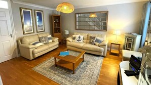 A living room with two sofas, a coffee table, a bookshelf, a lamp, and a laptop on a desk. - 2 Bed in Torquay (oc-bemews) (Torquay)