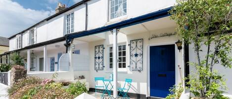 A white building with a blue door and a covered porch with blue chairs.