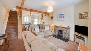 A cozy living room with a sofa, armchairs, a fireplace, a TV, and a kitchen in the background. - 2 Bed in Shaldon (oc-stchco) (Shaldon)