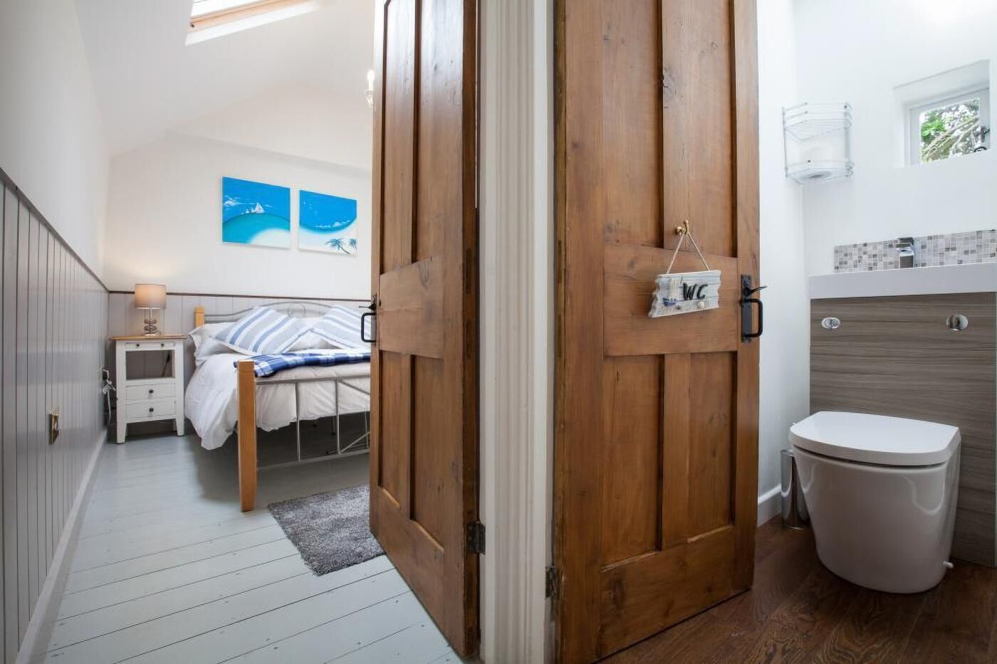 Ein Schlafzimmer mit einem Bett, einem Nachttisch mit Lampe und einer Holztür zu einem Badezimmer mit Toilette und Dusche.