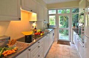 A kitchen with white cabinets, a countertop with fresh vegetables, and a view of greenery outside. - 1 Bed in Torquay (oc-kilmlo) (Torquay)
