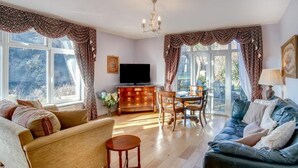 Un salon comprenant un canapé, une table à manger avec des chaises, un téléviseur et un lustre.