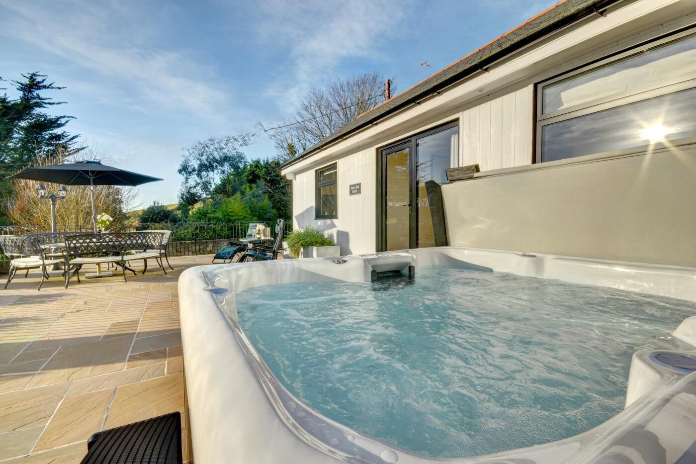 A hot tub with a patio area, outdoor furniture, and a building with large windows.