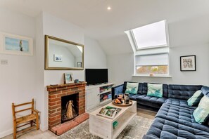 A living room with a fireplace, a sofa, a television, and a skylight.