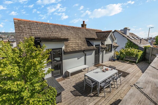 A residential property with a sloped roof, a patio with a table and chairs, and a white exterior wall.