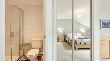 A bathroom with a toilet, shower, and a glass-enclosed closet leading to a bedroom with a bed and nightstands.
