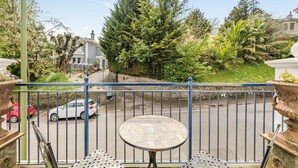 Een balkon met een ronde tafel en stoelen, met uitzicht op een straat met auto's en groen.