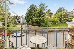 Ein Balkon mit rundem Tisch und Stühlen, der auf eine Straße mit Autos und Grünflächen blickt.