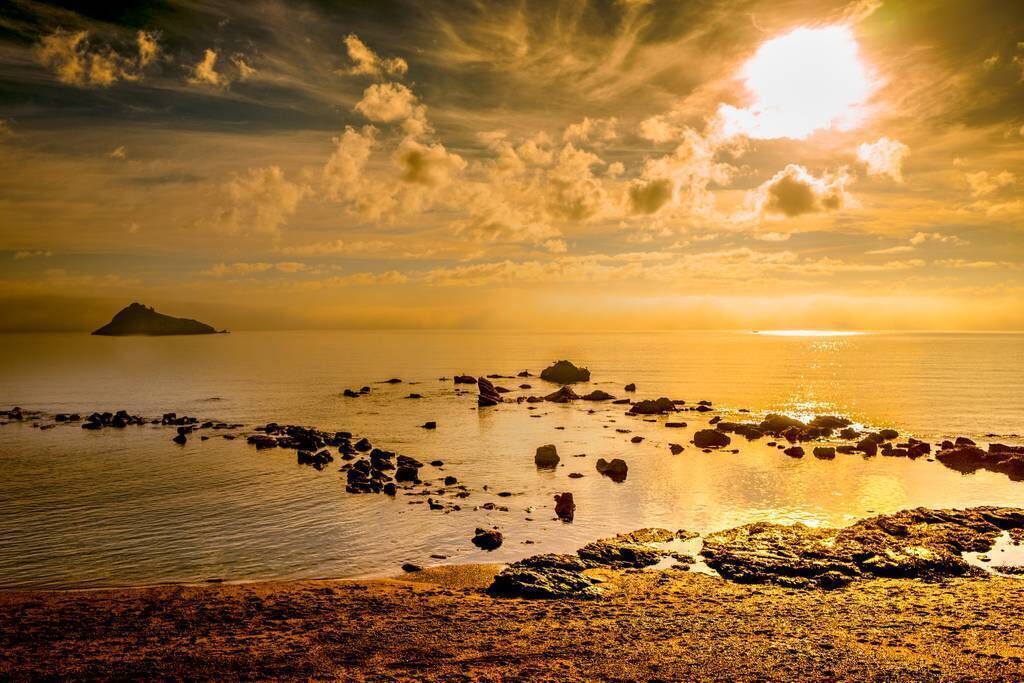 Un paysage côtier caractérisé par une rive rocheuse, une eau calme et une île visible au loin.