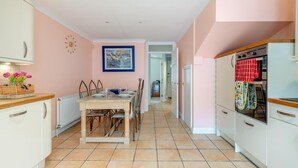 Een keuken met een eettafel, stoelen, een klok en een schilderij aan de muur.