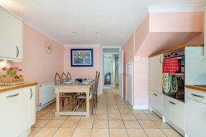 A kitchen with a dining table, chairs, a clock, and a painting on the wall.