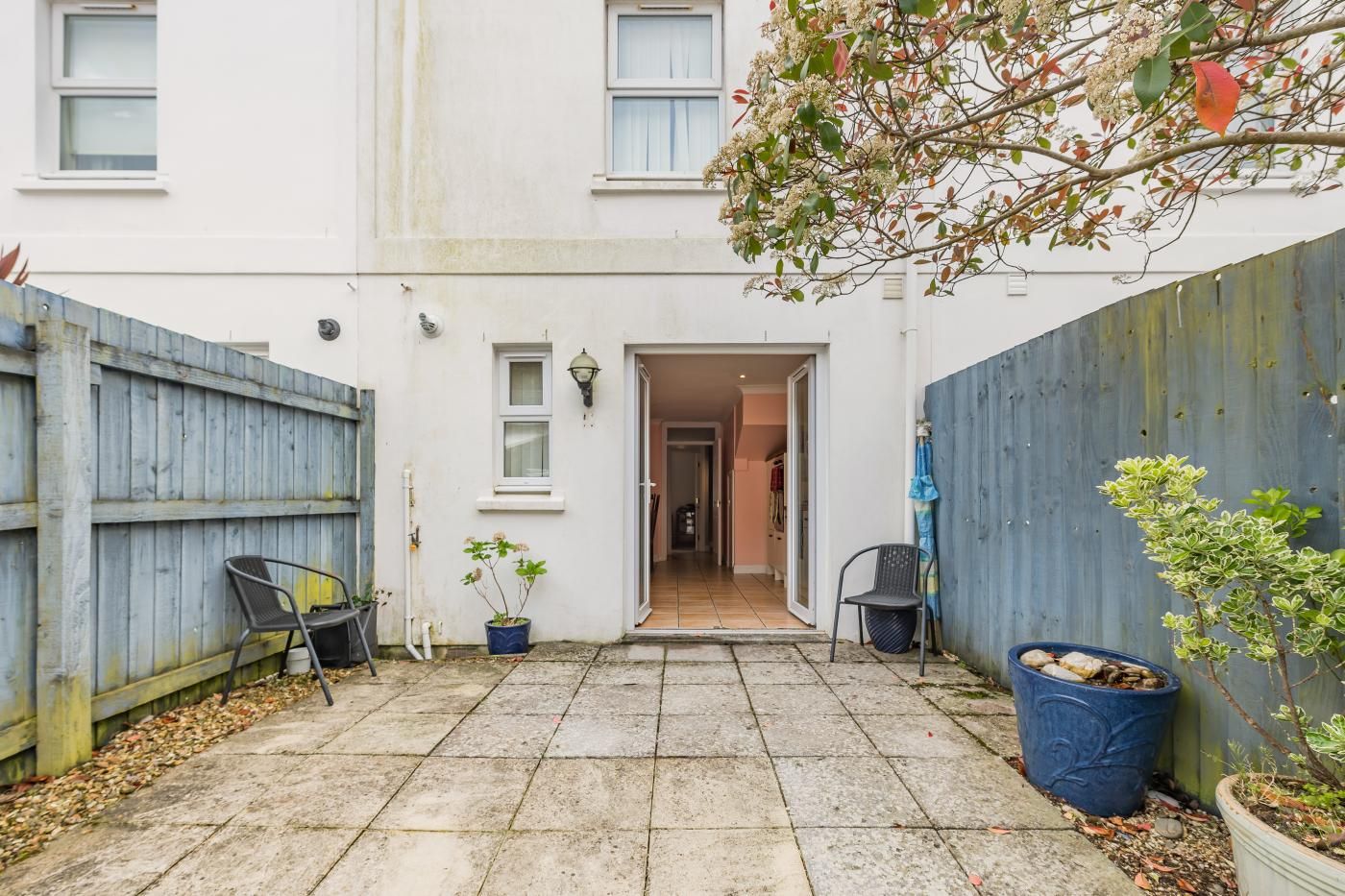 A courtyard with a wooden fence, a potted plant, and a chair.