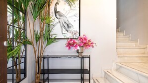 A hallway with a potted plant, a console table with a vase of flowers, and a staircase. - Genteel Home Mesones I (Granada)