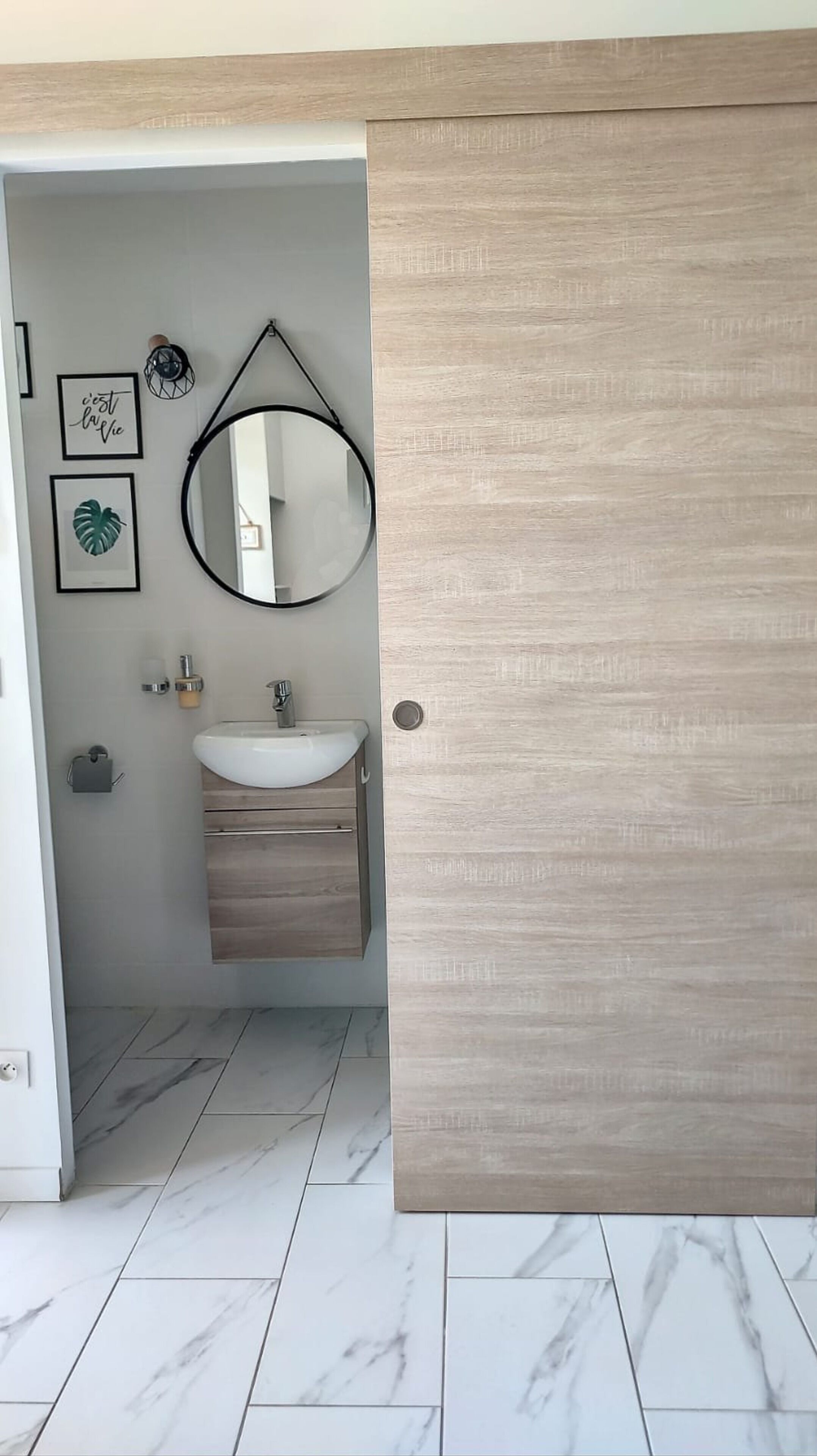 Een moderne badkamer met een houten wastafelmeubel, een ronde spiegel en een witte wasbak.