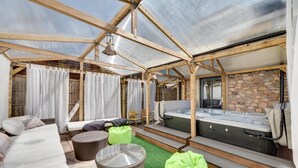 A glass-enclosed room with a hot tub, wicker furniture, and a stone wall.