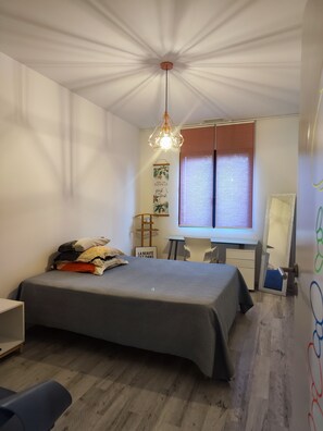 Une chambre à coucher comprenant un lit, un bureau, une chaise, un miroir et une fenêtre avec des stores.