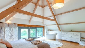 A bedroom with a large bed, a bathtub, and a white dresser. - 4 Bed in Drewsteignton (oc-bc2408) (Drewsteignton)