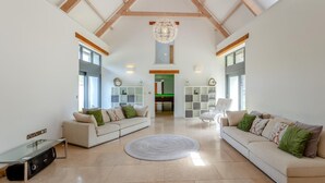 A spacious living room with high ceilings and exposed beams, two sofas with cushions, a glass coffee table, and a chandelier. - 4 Bed in Drewsteignton (oc-bc2408) (Drewsteignton)