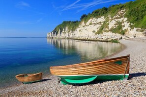 Een kiezelstrand met twee boten, een klif en een helderblauwe lucht.