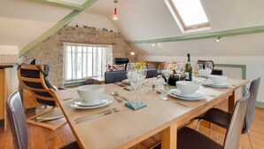Un coin repas avec une table en bois dressée pour quatre personnes, un mur en pierre et une lucarne.
