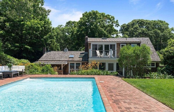 A two-story house with a swimming pool, surrounded by lush greenery.