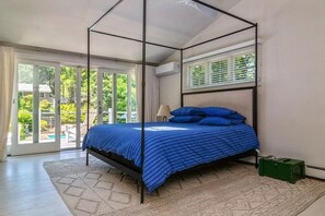 A bedroom with a four-poster bed, large windows, and a view of greenery outside.