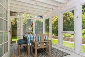 A conservatory with a table and chairs, large windows, and a patterned rug.