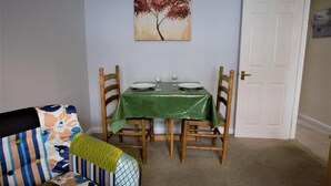 Un comedor con mantel verde, sillas de madera, un cuadro de un árbol y una puerta cerrada.