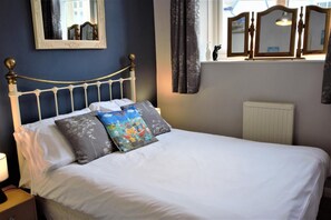 A neatly made bed with white linens and decorative pillows, a bedside lamp, and a window with curtains.