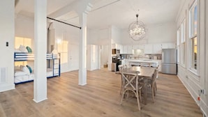 A spacious living area with a wooden floor, a dining table with chairs, and a kitchen with white cabinets and stainless steel appliances. - Charming Historic Loft in Downtown Galveston (Galveston)