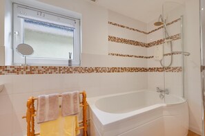 A bathroom with a bathtub, a shower, a window with a frosted glass, and a mirror.