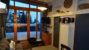 A cozy living room with a sofa, dining table, and chairs, a TV, and a large window with a view of trees and a snowy landscape. - 50m from ski slopes, 3rd floor, tv, ski locker, 35m², Les Arcs (Les Arcs)