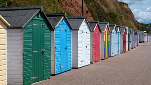 Une rangée de cabanes de plage aux couleurs vives, dotées de toits inclinés, s’étend le long d’une promenade dallée.