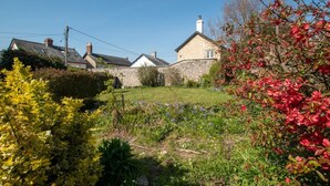 Une maison en pierre avec un jardin devant, entourée d’autres maisons.