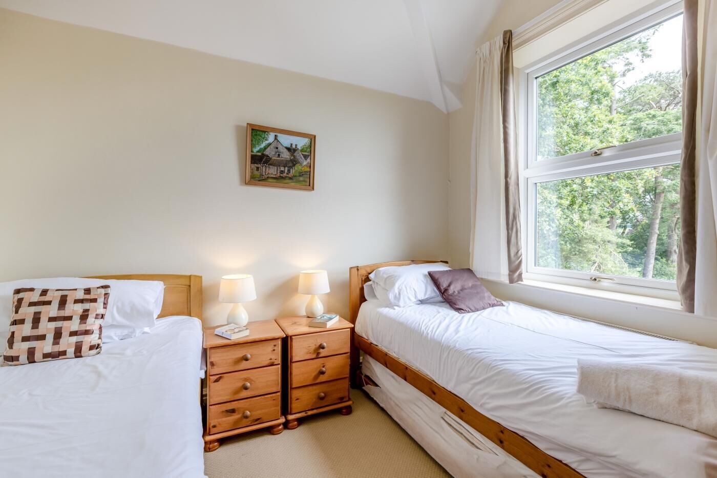 Une chambre avec deux lits, des tables de chevet en bois, des lampes de chevet, une fenêtre avec des rideaux et un tableau accroché au mur.