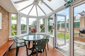 Ein Wintergarten mit Glasdach, einem runden Tisch und Stühlen sowie Blick auf einen Garten.