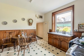 A kitchen with wooden cabinets, a dining table with chairs, a window with a view, and a clock on the wall.