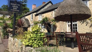 De Mason's Arms Inn in Branscombe, met stenen gebouwen, rieten parasols en terras.