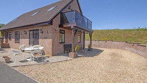 Een twee verdiepingen tellend huis met een patio, tuinmeubilair en een grindpad.