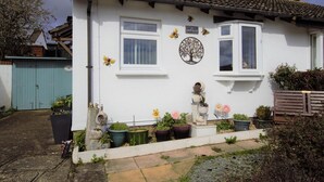Une maison blanche avec un toit en tuiles, un jardin agrémenté de plantes en pot et un portail bleu.