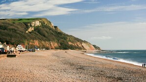 A pebble beach with a cliff and houses in the background. - 3 Bed in Seaton (oc-mbdal) (Seaton)