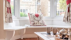 A cozy room with a bench by a window, a wooden table with a teapot and cups, and a decorative pillow. - 3 Bed in Seaton (oc-mbdal) (Seaton)
