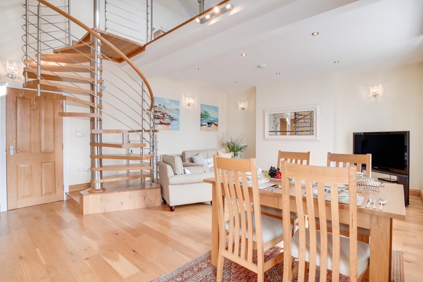 A modern interior with a spiral staircase, a dining area with wooden furniture, a sofa, and a flat-screen TV.