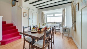 Un coin repas avec une table en bois dressée pour le repas, un escalier rouge et une vue par la fenêtre.