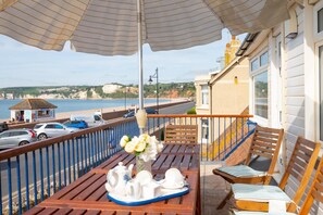 A balcony with a table set for tea, a chair, and a view of the sea and buildings. - 4 Bed in Seaton (oc-mbbrk) (Seaton)